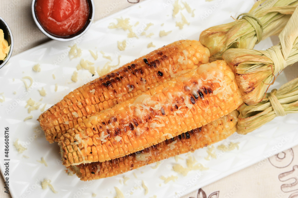 Grilled Sweet Corn with Butter and Shredded Mozarella. Served on White Plate