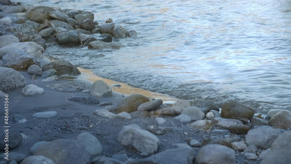 Small waves lapping on the riverside with rocks and sand in the cool shade Small waves lapping on the riverside with rocks and sand in the cool shade