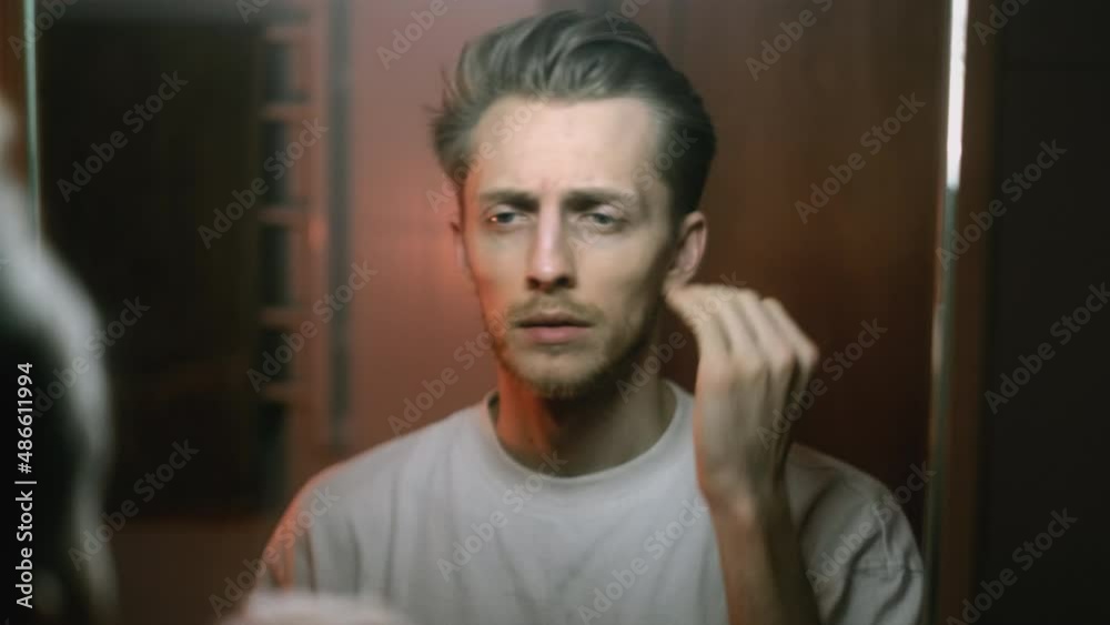 Young caucasian man standing the mirror in bath looking on himself and making hairstyle. Young caucasian man standing the mirror in bath looking on himself and making hairstyle.