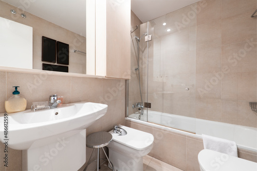 Modern restroom with dark brown tiled walls  shower  white toilet bowls and cream marble countertop in a vacation rental apartment