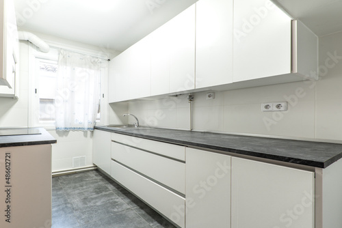 Furnished kitchen with elongated black countertop and plain white cabinets