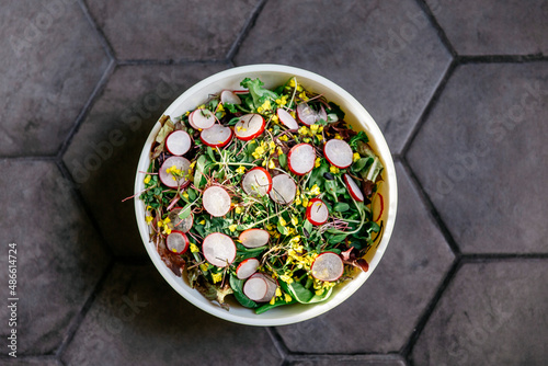 A green salad with edible flowers and radishes on a gray tile surface.