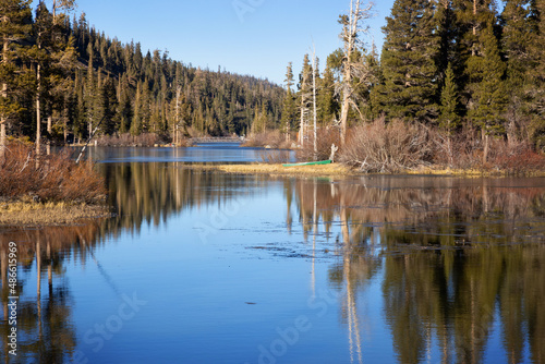 Green Canoe onshore at Twin Lakes in winter at Mammoth Lakes, California. Calm lake water with clear reflection of mountains and trees. Green canoe on grassy shore of idyllic lake.