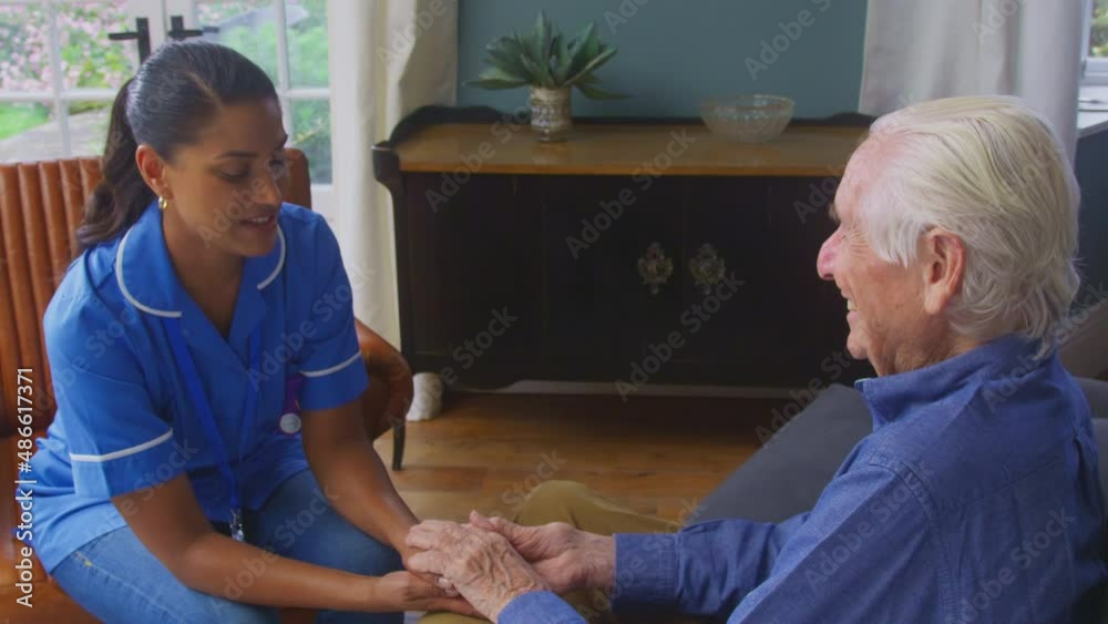 Female care worker in uniform holding hands of senior man sitting in care home lounge - shot in slow motion 