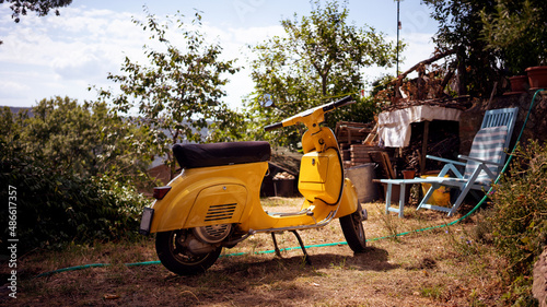 A yellow typical Italian motorbike in a backyard  photo