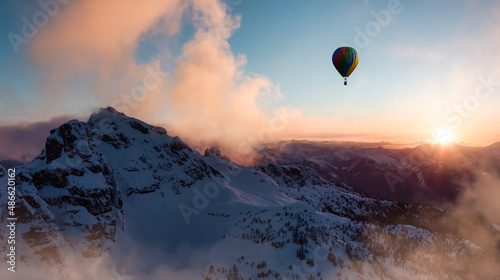 Dramatic Mountain Landscape covered in clouds and Hot Air Balloon Flying. Adventure Dream Concept Artwork Composite. Aerial Image from British Columbia, Canada. Sunset or Sunrise Sky