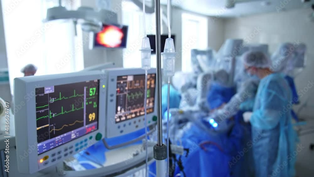 Technical equipment necessary for operations. Drop counters, screens and monitor for surgery. Surgeon at Da Vinci robot at backdrop in blur.