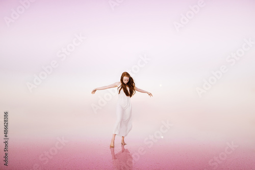 Red head woman with outstretched arms on the pink lake photo
