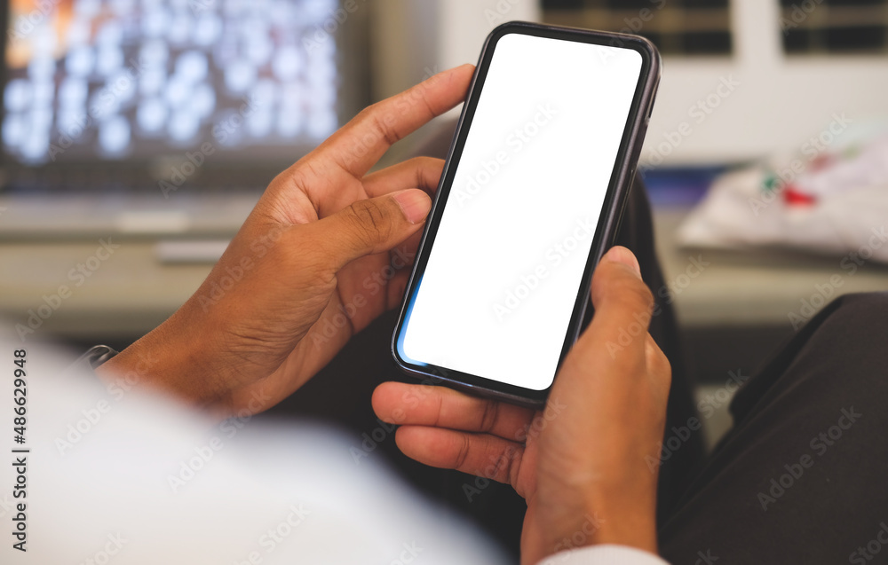 Over shoulder view of young man hands holding smart phone empty screen while sitting at workplace. Over shoulder view of young man hands holding smart phone empty screen while sitting at workplace.