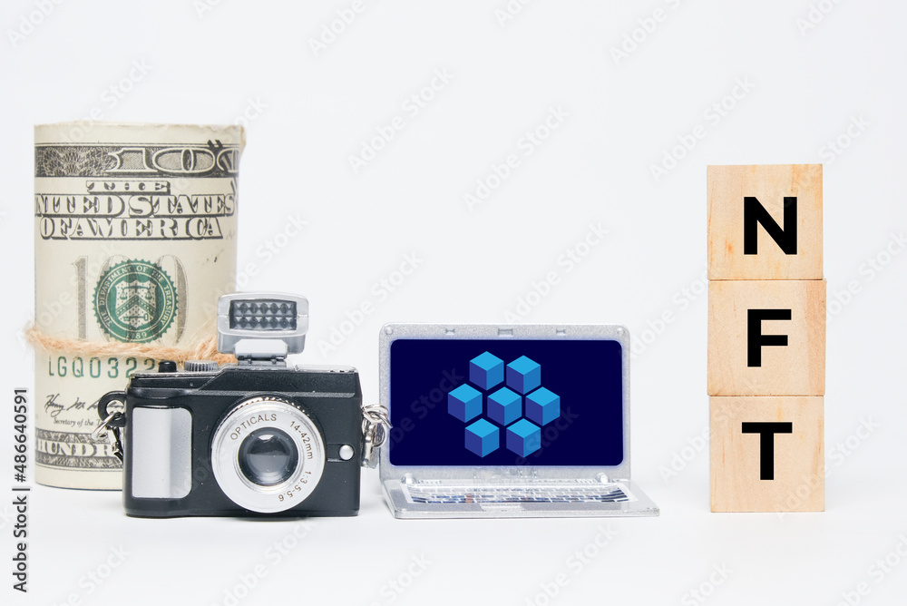 Obraz premium A miniature camera, laptop with blockchain, fake money and NFT word. A non-fungible token trading concept.