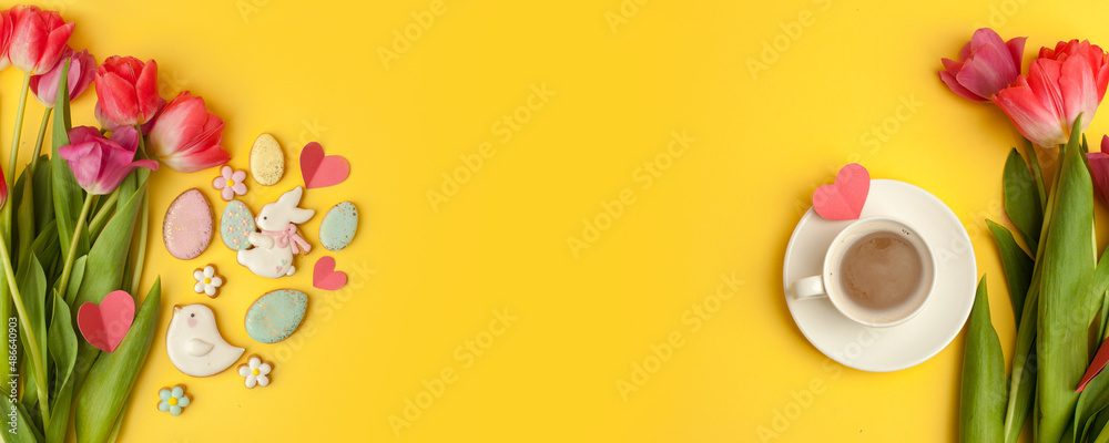 Easter gingerbread cookies, spring flowers, cup of coffee on yellow background. Cozy home Easter greeeting card concept, banner for your site, copy space top view, stylish composition