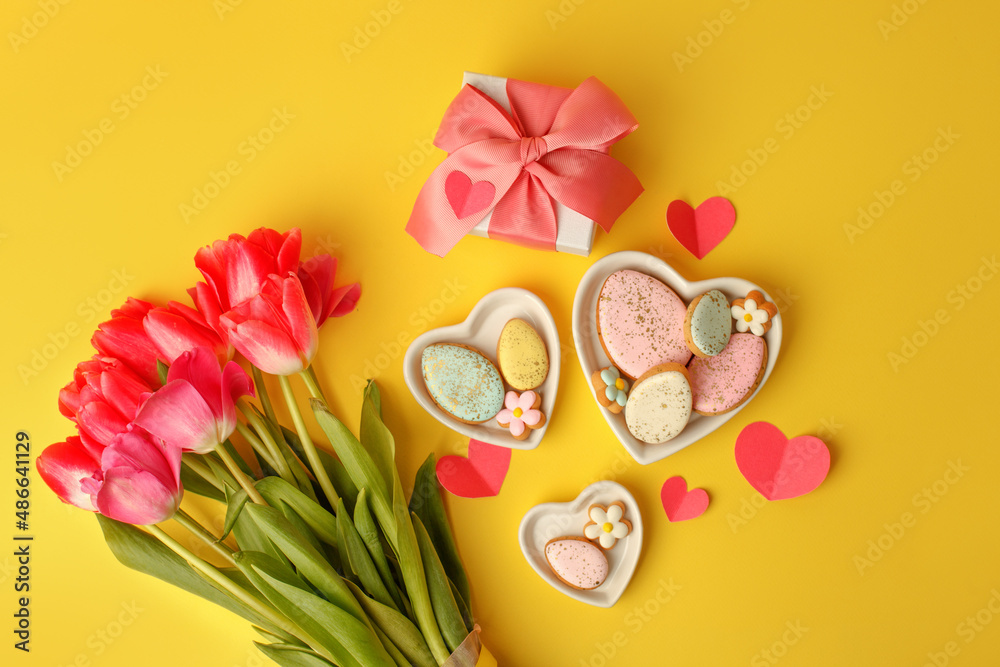Sweets, pastry, gingerbread cookies for Easter table. Easter eggs heart shaped decor plate, pink tulips on yellow background top view copy space, spring seasonal holiday banner for site, flyer, coupon