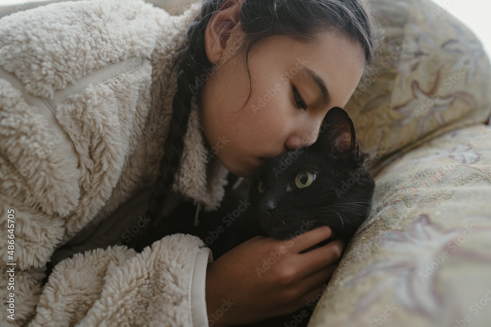 sweet girl with braids kissing black cat lying on couch sweet girl with braids kissing black cat lying on couch