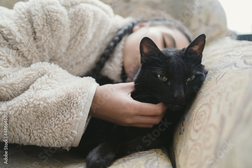 sweet girl pampering her black cat lying on the couch