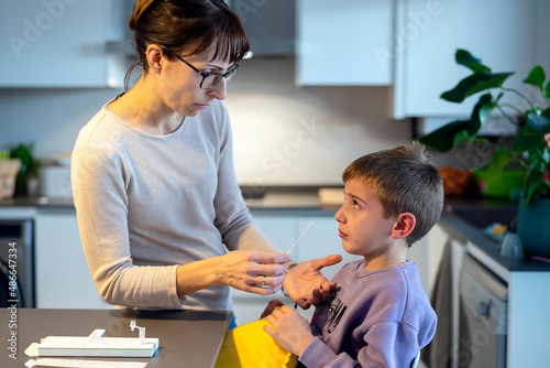 Mother and upset son doing antigen test in kitchen