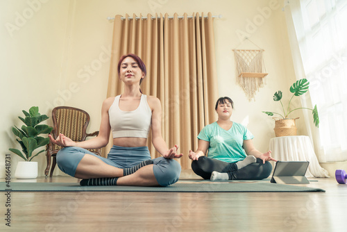 Two Asian women body size different in sport wear doing training meditation yoga at home together. Healthy lifestyle and workout at home concept.