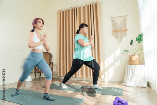 Two Asian women body size different in sport wear doing training yoga at home together. Healthy lifestyle and workout at home concept.