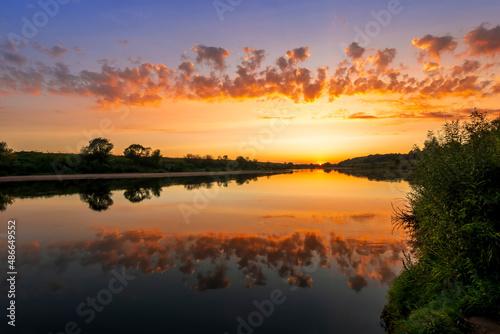 Amazing view at scenic landscape on a beautiful river and colorful sunset with reflection on water surface and glow on a background, spring season landscape © Yaroslav