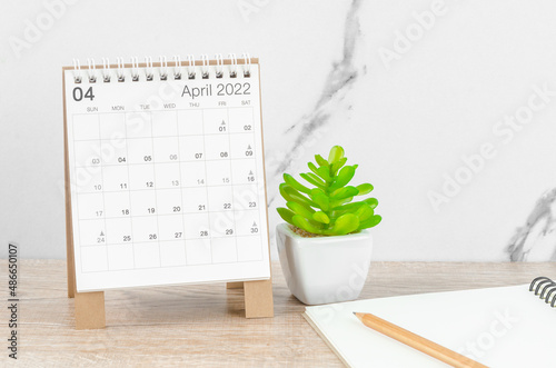 April 2022 desk calendar with plant on wooden table.