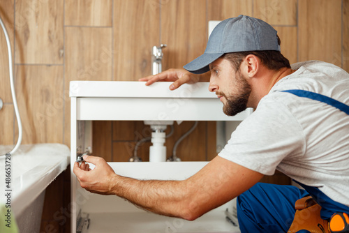 Concentrated plumber, male worker in uniform fixing sink and water pipe in the bathroom