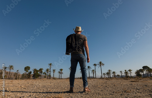 Adult man in cowboy hat on Tabernas desert with palm trees against blue sky. Almeria, Spain