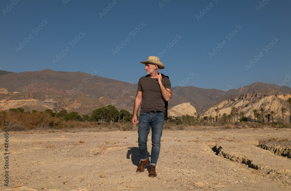 Adult man in cowboy hat on Tabernas desert with palm trees against blue sky. Almeria, Spain Adult man in cowboy hat on Tabernas desert with palm trees against blue sky. Almeria, Spain