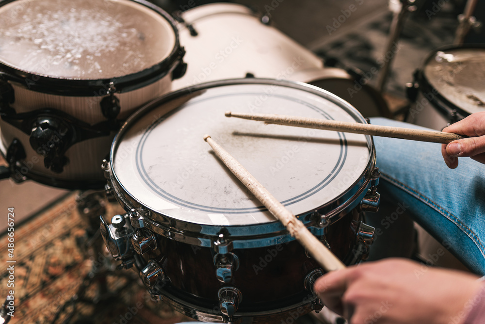 High angle of crop anonymous male musician in jeans playing drum kit and creating rhythm in garage