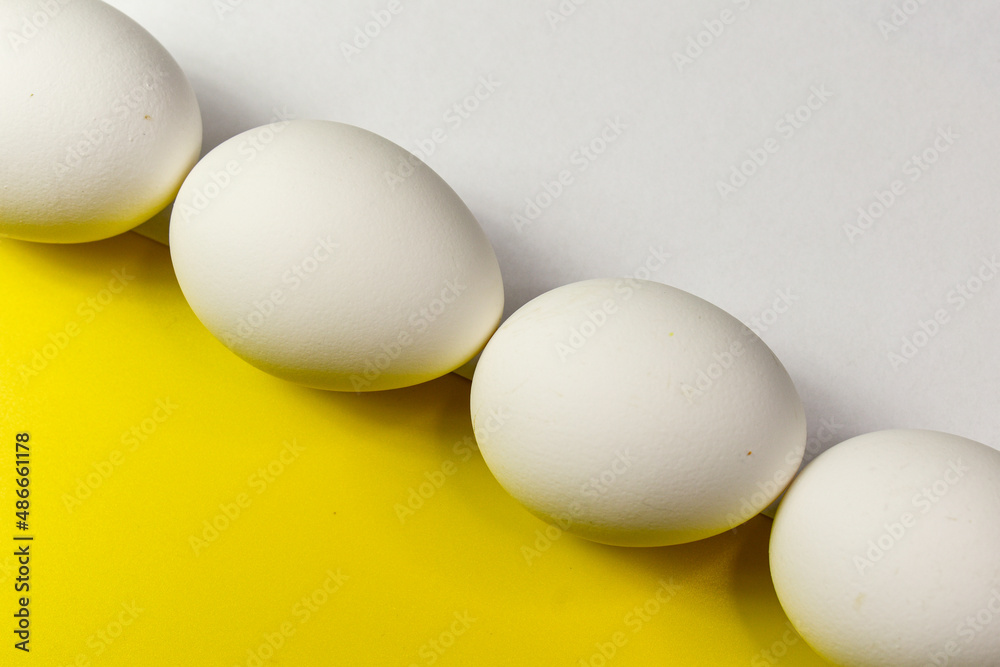 A composition of white chicken eggs laid diagonally between a yellow and white background