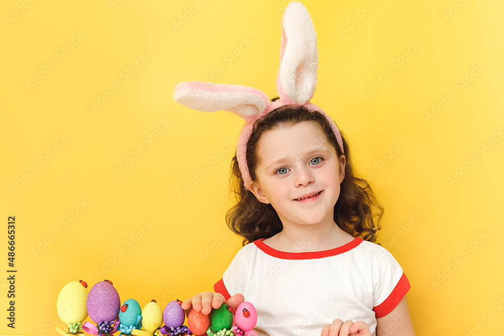 Portrait of cheerful little girl wears fluffy ears, happy looking at camera, standing near easter eggs, isolated on yellow studio background with copy space. Happy moments. Easter and holiday concept Portrait of cheerful little girl wears fluffy ears, happy looking at camera, standing near easter eggs, isolated on yellow studio background with copy space. Happy moments. Easter and holiday concept