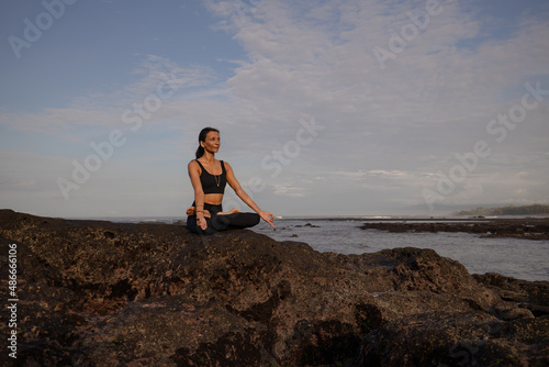 Morning meditation yoga on the beach. Asian woman sitting on the rock in Lotus pose. Padmasana. Hands in gyan mudra. Yoga retreat. Healthy concept. Copy space. Mengening beach  Bali
