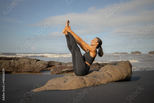 Outdoor yoga practice. Slim Asian woman practicing Ubhaya Padangusthasana, Wide-Angle Seated Forward Bend. Strengthen legs and core. Self care concept. Yoga retreat. Mengening beach, Bali photo