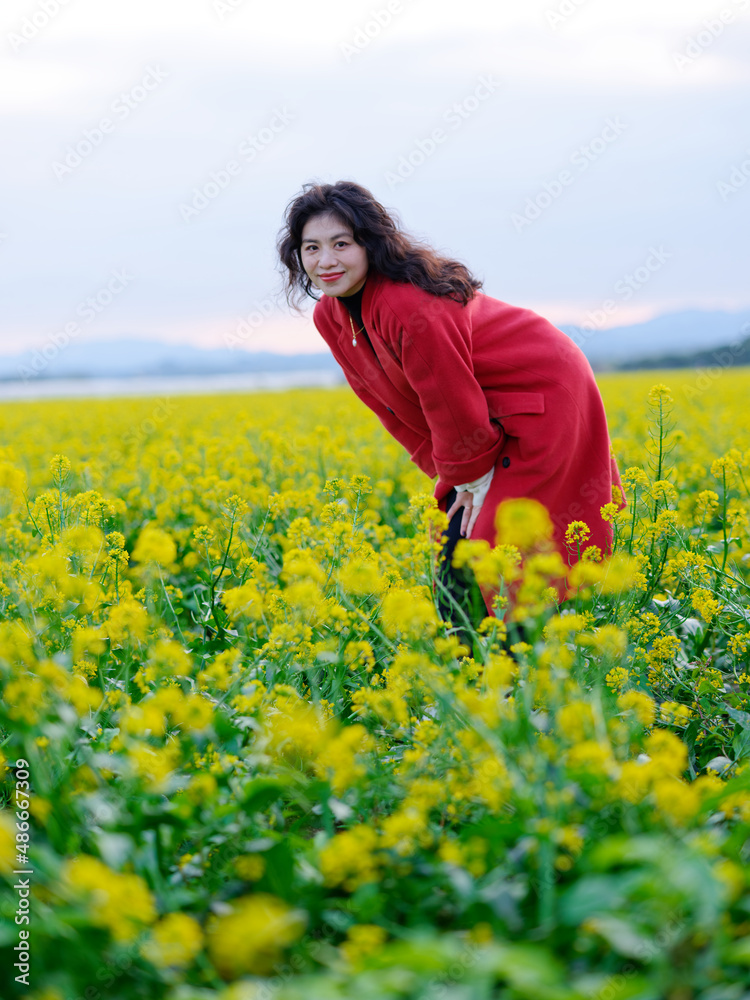 An Asian woman in a red trench coat stands in a field of rape flowers