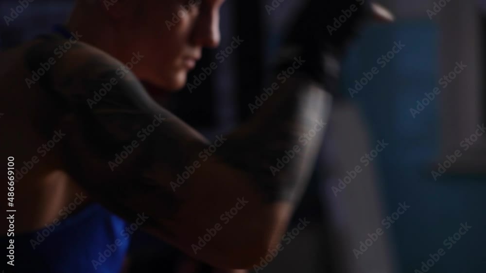 Close-up trackins shot of boxer male punching air with fists training warm-up before boxing workout in sport club with dark interior. Strong kickboxer getting ready for fight in fitness center. Close-up trackins shot of boxer male punching air with fists training warm-up before boxing workout in sport club with dark interior. Strong kickboxer getting ready for fight in fitness center.