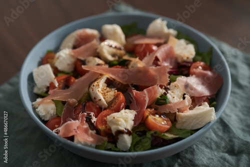 Fresh salad with prosciutto, mozzarella and cherry tomatoes in blue bowl
