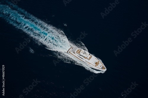 Large white super boat moves on the water leaving a white trail on the water aerial view. Luxury white mega yacht fast movement on dark water in the ocean top view. Big yacht in the sea drone view © Berg
