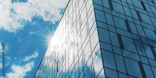sunlight shines from behind office building with panoramic windows against blue sky with cumulus white clouds