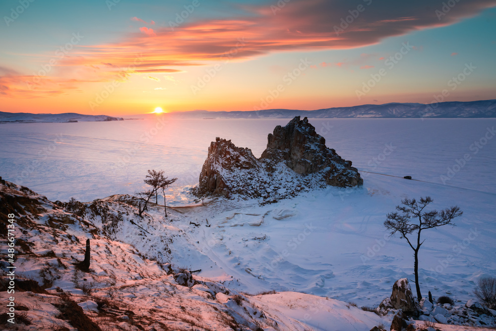 Frozen Baikal lake in winter. Shamanka rock on Olkhon island at sunset. Famous nature landmark in Baikal, Siberia, Russia.