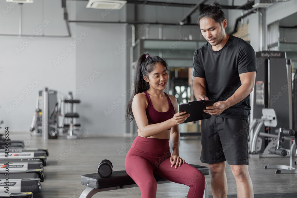 Obraz premium Asian woman exercise with personal trainer in gym. Personal trainer showing and talking about exercise plan with healthy woman.