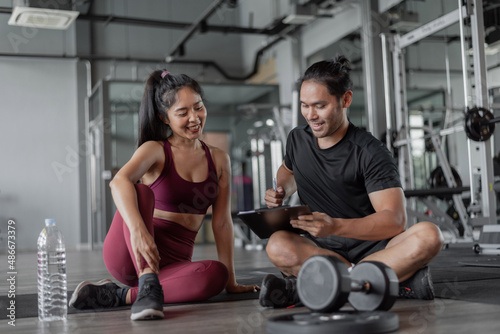 Asian woman exercise with personal trainer in gym. Personal trainer showing and talking about exercise plan with healthy woman.