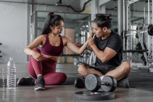 Asian woman exercise with personal trainer in gym. healthy woman talking with personal trainer in fitness.
