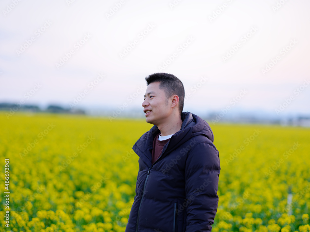 A boy in a black down jacket stands in a field of rape flowers
