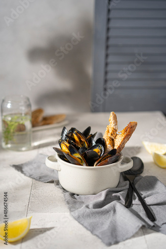 Cooked, boiled mussels with lemon juice, parsley and toasted bread in white bowl (plate) on the table. Seafood, copy space. 
