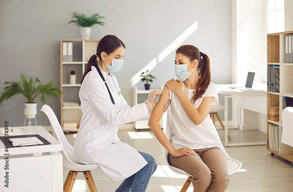 Fototapeta premium Female doctor or nurse vaccinate young woman patient in clinic. Woman GP make injection give vaccination against covid-19 corona virus to girl client in hospital. Coronavirus, healthcare, medicine.