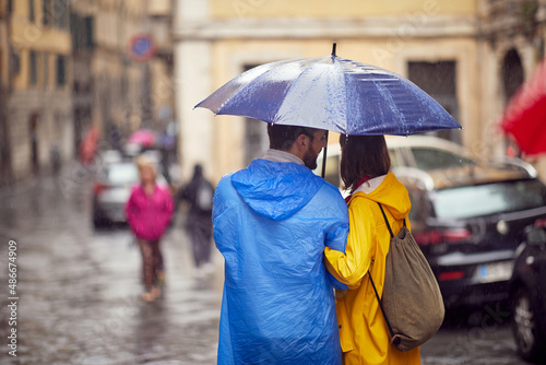 Shot from back of a young couple in love who is walking the city on a rainy day. Walk, rain, city, relationship