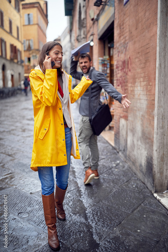 A young woman walking on the street and talking on the phone on a rainy day and does not care about passerby she hit. Walk, rain, city