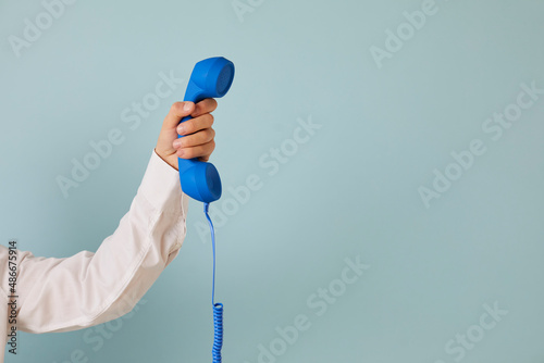 Human hand holding retro phone receiver against copy space background. Cropped shot of young man holding blue landline telephone receiver on light blue copyspace background. Customer support concept photo