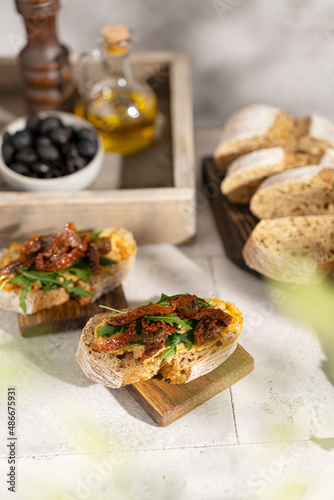 Ciabatta bread sandwich with humus and dried tomatoes, arugula leaves on white table. Italian traditional food - bruschetta, antipasto. with ingredients. Copy space. 