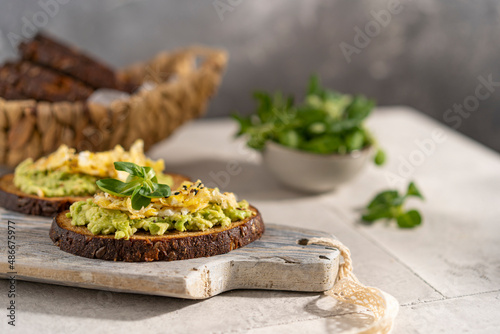 Avocado and egg sandwich with whole grain brown bread and greens, healthy diet vegan food. Breakfast on wooden board, white table. Copy space.