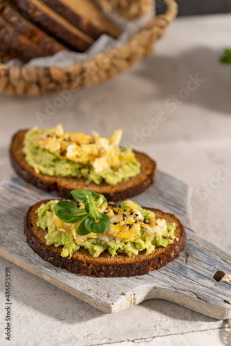 Avocado and egg sandwich with whole grain brown bread and greens, healthy diet vegan food. Breakfast on wooden board, white table. Copy space.