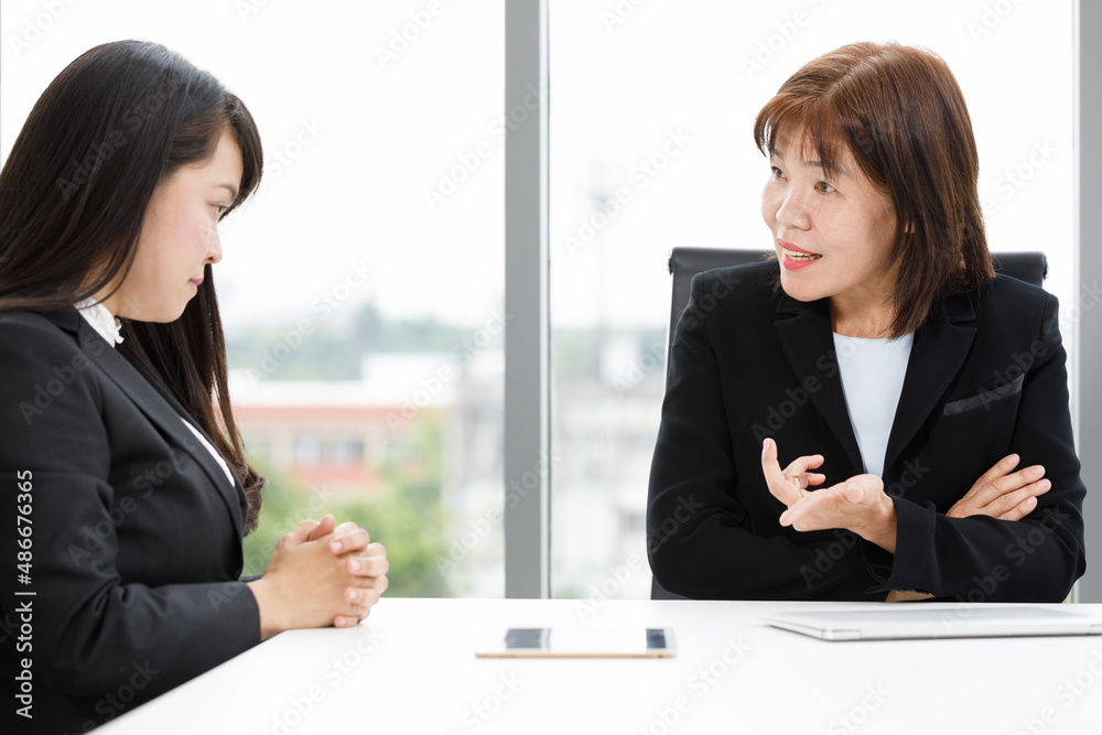 Asian professional successful senior female businesswoman manager in formal suit sitting smiling showing thumb up complimenting happy colleague employee at office working table when job achievement